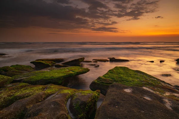 Calm ocean long exposure. Stones covered by geen moss in mysterious mist of the sea waves. Concept of nature background. Sunset scenery background. Soft focus. Mengening beach, Bali, Indonesia.