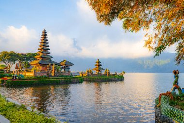 Bali adasındaki Pura Ulun Danu Bratan tapınağı. Güzel bale tapınağı. Bali 'nin simgesi. Bulutlu gökyüzü. Su yansıması. Ağaç dalları olan bir ön plan. Bratan Gölü, Bedugul, Bali, Endonezya