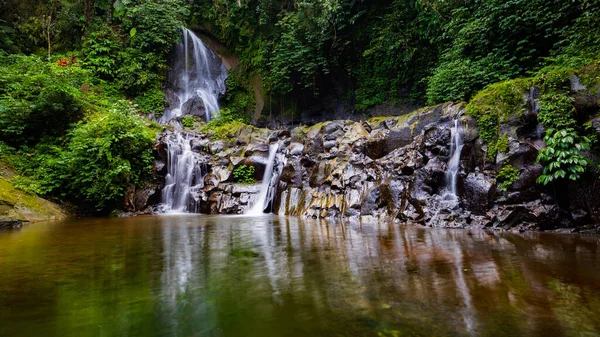 Waterfall landscape. Beautiful hidden Pengibul waterfall in rainforest. Water reflection. Tropical scenery. Slow shutter speed, motion photography. Nature background. Horizontal layout. Bali Indonesia