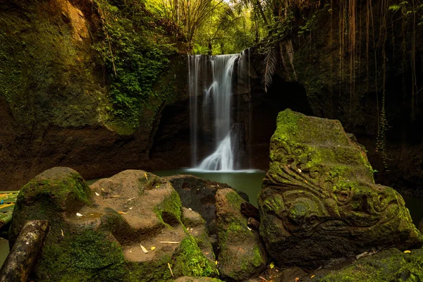 Waterfall landscape. Beautiful hidden waterfall in tropical rainforest. Foreground with big stones. Slow shutter speed, motion photography. Travel and adventure. Suwat waterfall, Bali, Indonesia