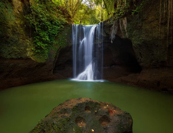 Waterfall landscape. Beautiful hidden waterfall in tropical rainforest. Foreground with big stone. Slow shutter speed, motion photography. Travel and adventure. Suwat waterfall, Bali, Indonesia
