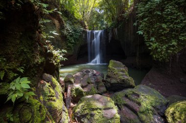 Şelale manzarası. Tropikal yağmur ormanlarında saklı güzel bir şelale. Büyük taşlı ön plan. Yavaş deklanşör hızı, hareket fotoğrafçılığı. Seyahat ve macera. Suwat Şelalesi, Bali, Endonezya