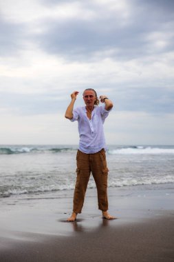 Sahilde yalınayak duran yalnız bir adam. Kahverengi pantolon ve beyaz gömlek giyen bir adam. Horizon deniz manzarası. Bulutlu gökyüzü. Seyahat konsepti. Uzayı kopyala Asya 'da tatil. Bali, Endonezya