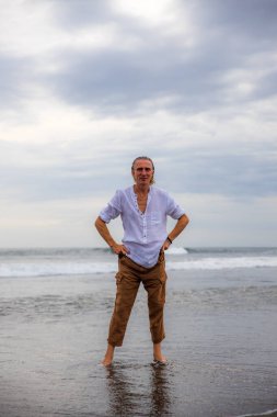 Sahilde yalınayak duran yalnız bir adam. Kahverengi pantolon ve beyaz gömlek giyen bir adam. Horizon deniz manzarası. Bulutlu gökyüzü. Seyahat konsepti. Uzayı kopyala Asya 'da tatil. Bali, Endonezya
