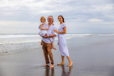 Mutlu aile kumsalda vakit geçiriyor. Yaz tatili. Aile tatili. Anne, baba ve kız sahilde yalınayak yürüyor. Baba, kızını kollarında taşıyor. Uzayı kopyala Bali, Endonezya