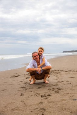 Kızı babaya sarılıyor. Kumda çömelmiş bir adam. Baba ve kızı arasındaki ilişki. Aile kavramı. Kumsalda birlikte vakit geçirin. Asya 'da yaz tatili. Uzayı kopyala Bali, Endonezya