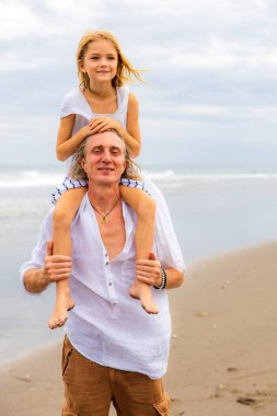 Babasının omuzlarında oturan bir kız. Baba ve kızı sahilde birlikte oynuyorlar. Mutlu bir aile. Birlikte eğleniyoruz. Kaliteli zaman. Yaz tatili. Asya 'da tatil. Aile bağları. Bali