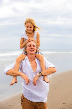 Babasının omuzlarında oturan bir kız. Baba ve kızı sahilde birlikte oynuyorlar. Mutlu bir aile. Birlikte eğleniyoruz. Kaliteli zaman. Yaz tatili. Asya 'da tatil. Aile bağları. Bali