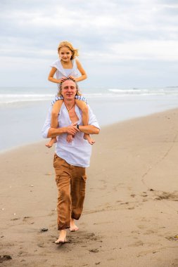 Babasının omuzlarında oturan bir kız. Baba ve kızı sahilde birlikte oynuyorlar. Mutlu bir aile. Birlikte eğleniyoruz. Kaliteli zaman. Yaz tatili. Asya 'da tatil. Aile bağları. Bali