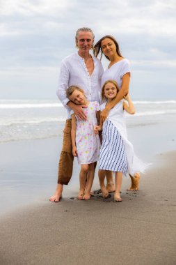 Kumsalda mutlu bir aile. Anne, baba ve kızları birlikte güzel vakit geçiriyorlar. Yaz tatili. Asya 'da aile tatili. Aileler çocukları kucaklıyor. Seyahat konsepti. Uzayı kopyala Bali, Endonezya