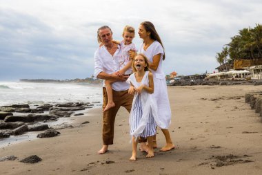 Kumsalda mutlu bir aile. Anne, baba ve kızları birlikte güzel vakit geçiriyorlar. Kız korkunç suratlar yapıyor, kameraya bakıyor, dilini dışarı çıkarıyor. Yaz tatili. Aile tatili. Bali