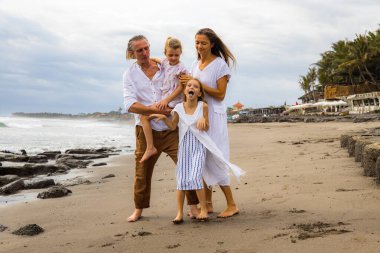 Kumsalda mutlu bir aile. Anne, baba ve kızları birlikte güzel vakit geçiriyorlar. Kız korkunç suratlar yapıyor, kameraya bakıyor, dilini dışarı çıkarıyor. Yaz tatili. Aile tatili. Bali
