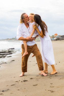 Kumsalda mutlu bir aile. Ebeveynler kızını öpüyor. Anne, baba ve kızı birlikte güzel vakit geçiriyorlar. Yaz tatili. Asya 'da aile tatili. Bali, Endonezya