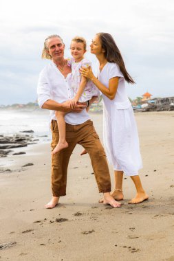 Kumsalda mutlu bir aile. Anne kucağı kızı. Baba, kızını kollarında taşıyor. Birlikte güzel vakit geçirmek. Çıplak ayakla yürüyorum. Yaz tatili. Asya 'da tatil. Bali Adası, Endonezya