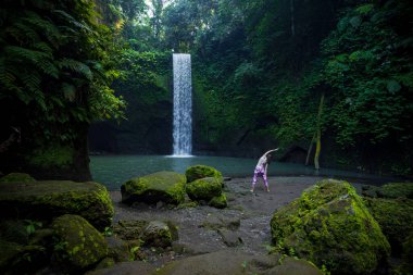 Beyaz kadın, Watelfall yakınlarında yoga yapıyor. Trikonasana, Üçgen Poz. Asana ayakta duruyor. Bağışıklık sistemini destekleyin. Yoga inzivası. Sağlık konsepti. Arkadan bak. Tibumana şelalesi, Bali