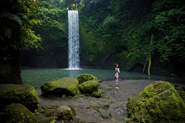 户外瑜伽练习 站在瀑布边的年轻女子 手握着纳马斯特泥巴 闭上眼睛 准备向太阳致敬苏里亚 纳马斯卡 平静的心情 瑜伽撤退 巴厘Tibumana瀑布 — 图库照片