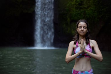 Namaste mudra. Kapatın. Şelalenin yanındaki yoga. Kadın meditasyon yapıyor, yoga yapıyor ve namaste Mudra ile pranayama yapıyor. Yoga açık hava konsepti. Ön manzara. Bali 'de geri çekiliyoruz. Tibumana şelalesi. Boşluğu kopyala.
