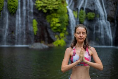 Namaste mudra. Kapatın. Şelalenin yanındaki yoga. Genç bir kadın meditasyon yapıyor, yoga yapıyor ve namaste Mudra ile pranayama yapıyor. Yoga açık hava konsepti. Uzayı kopyala Bali 'de geri çekiliyoruz. Banyumala Şelalesi.