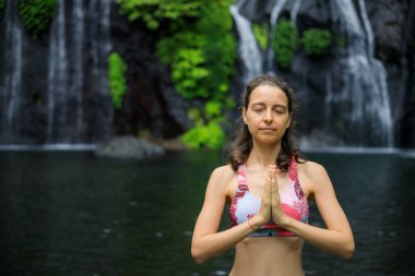 Namaste mudra. Kapatın. Şelalenin yanındaki yoga. Genç bir kadın meditasyon yapıyor, yoga yapıyor ve namaste Mudra ile pranayama yapıyor. Yoga açık hava konsepti. Uzayı kopyala Bali 'de geri çekiliyoruz. Banyumala Şelalesi.
