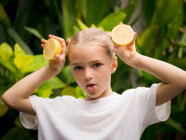İki dilim taze limonu olan güzel bir kız. Kafkasyalı kız limonu kafasının yanında tutuyor, dilini gösteriyor. Meyveye odaklan. Yeşil tropik yapraklar arka planda. Organik meyve konsepti. Bali