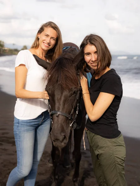 Two beautiful women hugging brown horse. Horse riding on the beach. Human and animals relationship. Nature concept. Copy space. Bali, Indonesia