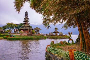 Bali adasındaki Pura Ulun Danu Bratan tapınağı. Güzel bale tapınağı. Bali 'nin simgesi. Bulutlu gökyüzü. Su yansıması. Bambu dallı ön plan. Bratan Gölü, Bedugul, Bali, Endonezya