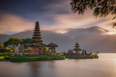 Bali adasındaki Pura Ulun Danu Bratan tapınağı. Güzel bale tapınağı. Bali 'nin simgesi. Bulutlu gökyüzü. Su yansıması. Bambu dallı ön plan. Bratan Gölü, Bedugul, Bali, Endonezya