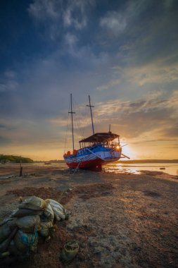 Okyanus kıyısında terk edilmiş eski bir gemi. Bozuk gemi. Kumsal. Gün batımı manzarası. Bulutlu gökyüzü. Güneş ufukta görünüyor. Dikey yerleşim. Uzayı kopyala Benoa Limanı, Bali, Endonezya.