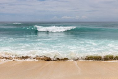 Deniz manzaralı arka plan. Kumsal, süt köpüğü dalgaları, mavi okyanus. Manzaralı su manzarası. Ufuk çizgisi. Bulutlu gökyüzü. Doğa ve çevre kavramı. Gün ışığı. Uzayı kopyala Rüya Diyarı Sahili, Bali Endonezya