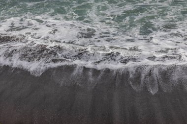 Waterscape arka planı. Beyaz süt köpüklü dalgalı siyah kumsal. Doğa ve çevre kavramı. Siyah ve beyaz kontrastı. Gün ışığı. Uzayı kopyala Endonezya, Bali 'deki volkanik plaj
