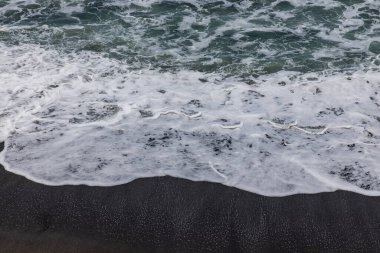 Waterscape arka planı. Beyaz süt köpüklü dalgalı siyah kumsal. Doğa ve çevre kavramı. Siyah ve beyaz kontrastı. Gün ışığı. Uzayı kopyala Endonezya, Bali 'deki volkanik plaj