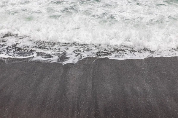 Waterscape arka planı. Beyaz süt köpüklü dalgalı siyah kumsal. Doğa ve çevre kavramı. Siyah ve beyaz kontrastı. Gün ışığı. Uzayı kopyala Endonezya, Bali 'deki volkanik plaj