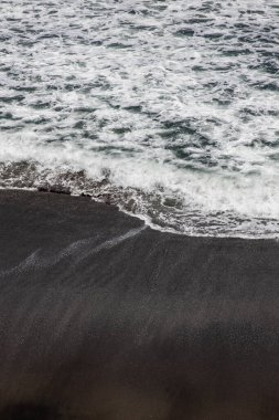 Waterscape arka planı. Beyaz süt köpüklü dalgalı siyah kumsal. Doğa ve çevre kavramı. Siyah ve beyaz kontrastı. Gün ışığı. Uzayı kopyala Endonezya, Bali 'deki volkanik plaj