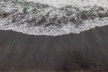 Waterscape arka planı. Beyaz süt köpüklü dalgalı siyah kumsal. Doğa ve çevre kavramı. Siyah ve beyaz kontrastı. Gün ışığı. Uzayı kopyala Endonezya, Bali 'deki volkanik plaj