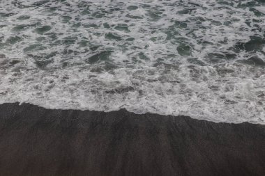 Waterscape arka planı. Beyaz süt köpüklü dalgalı siyah kumsal. Doğa ve çevre kavramı. Siyah ve beyaz kontrastı. Gün ışığı. Uzayı kopyala Endonezya, Bali 'deki volkanik plaj