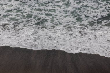 Waterscape arka planı. Beyaz süt köpüklü dalgalı siyah kumsal. Doğa ve çevre kavramı. Siyah ve beyaz kontrastı. Gün ışığı. Uzayı kopyala Endonezya, Bali 'deki volkanik plaj