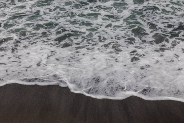 Waterscape arka planı. Beyaz süt köpüklü dalgalı siyah kumsal. Doğa ve çevre kavramı. Siyah ve beyaz kontrastı. Gün ışığı. Uzayı kopyala Endonezya, Bali 'deki volkanik plaj