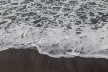 Waterscape arka planı. Beyaz süt köpüklü dalgalı siyah kumsal. Doğa ve çevre kavramı. Siyah ve beyaz kontrastı. Gün ışığı. Uzayı kopyala Endonezya, Bali 'deki volkanik plaj