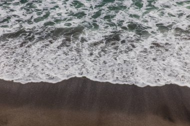 Waterscape arka planı. Beyaz süt köpüklü dalgalı siyah kumsal. Doğa ve çevre kavramı. Siyah ve beyaz kontrastı. Gün ışığı. Uzayı kopyala Endonezya, Bali 'deki volkanik plaj