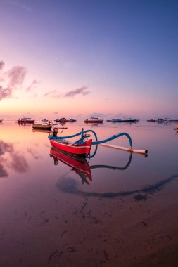 Deniz Burnu. Balıkçı teknesi. Geleneksel Balili tekne jukung. Gün doğarken sahilde balıkçı teknesi. Su yansıması. Renkli gökyüzü. Ufukta güneş ışığı görünüyor. Kapama hızı yavaş. Yumuşak odaklanma. Sanur, Bali