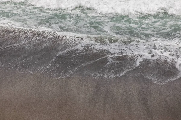 Waterscape arka planı. Beyaz süt köpüklü dalgalı siyah kumsal. Doğa ve çevre kavramı. Siyah ve beyaz kontrastı. Gün ışığı. Uzayı kopyala Endonezya, Bali 'deki volkanik plaj