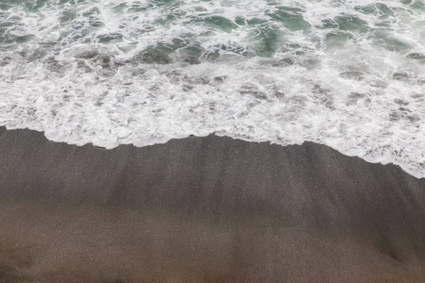 Waterscape arka planı. Beyaz süt köpüklü dalgalı siyah kumsal. Doğa ve çevre kavramı. Siyah ve beyaz kontrastı. Gün ışığı. Uzayı kopyala Endonezya, Bali 'deki volkanik plaj