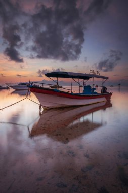 Okyanusta bir tekne. Gün doğumu manzaralı. Dalgalar çekildi. Ufuk çizgisinde güneş ışığı. Bulutlu gökyüzü. Su yansıması. Yumuşak odaklanma. Kapama hızı yavaş. Uzayı kopyala Dikey yerleşim. Sanur Plajı, Bali, Endonezya