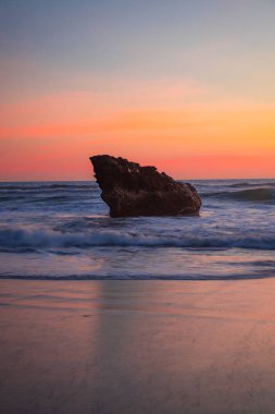 Gün batımı deniz manzarası. Okyanusta taş gibi. Kapama hızı yavaş. Yumuşak odaklanma. İpeksi su. Pembe gökyüzü. İnanılmaz bir su yansıması. Doğa ve çevre geçmişi. Uzayı kopyala Endonezya, Bali Plajı.