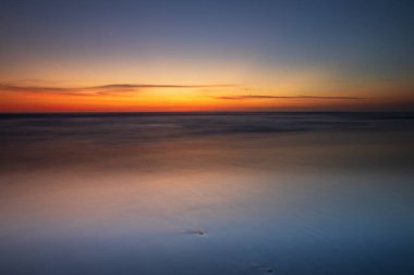 Gün batımı deniz manzarası. Kapama hızı yavaş. Yumuşak odaklanma. İpeksi su. Siyah kum plajı. Renkli gökyüzü. İnanılmaz bir su yansıması. Doğa ve çevre geçmişi. Uzayı kopyala Endonezya, Bali 'de Günbatımı.
