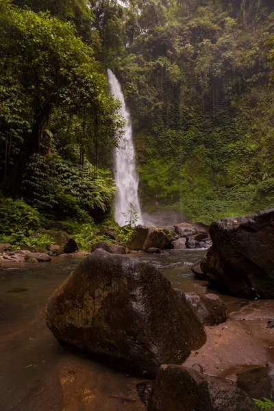 Şelale manzarası. Tropikal yağmur ormanlarında saklı güzel bir şelale. Büyük taşlı ön plan. Yavaş deklanşör hızı, hareket fotoğrafçılığı. Seyahat ve macera. Nung Nung Şelalesi, Bali, Endonezya