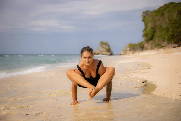 Bhujapidasanaを練習白人女性 ビーチで腕の圧力バランス 強い健康体だ セルフケアの概念 ヨガの隠れ家だ インドネシアのバリのトーマスビーチ — ストック写真