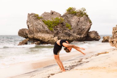 Bali plaj yogası. Hasta Uttanasana 'nın varyasyonu, Yükseltilmiş Kollar Pozu. Vücuttaki enerjiyi arttırır. Sırtın güçlü. Esnek omurga. Kişisel bakım konsepti. Bağışıklık sistemini destekleyin. Yoga inzivası. Thomas Plajı Bali Endonezya