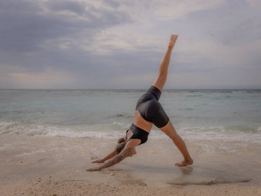 Bali 'de yoga. Genç kadın Eka Pada Adho Mukha Svanasana, Tek Ayaklı İt. Sağlam vücut, düz sırt. Sağlıklı bir yaşam tarzı. Okyanus manzaralı. Yoga inzivası. Uzayı kopyala Thomas Sahili, Bali