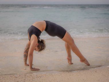 Bali yogası. Beyaz kadın Chakrasana ya da Urdhva Dhanurasana, Full Wheel Poose. Yukarı bakan yay pozisyonu derin bir arka virajdır. Esnek ve güçlü bir vücut. Zen hayatı. Thomas Sahili, Bali, Endonezya